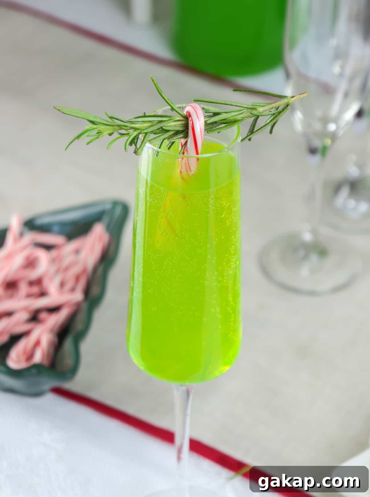 Green Grinch Mimosa Cocktail Recipe for Holiday Brunch 5 Green mimosa in a champagne glass with rosemary any mini candy cane.