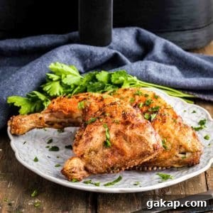 Crispy Air Fryer Chicken Leg Quarters with Garlic Herb Rub 8 Side shot of two chicken quarters garnished with herbs on a white plate on a wooden table and a blue cloth in the background.