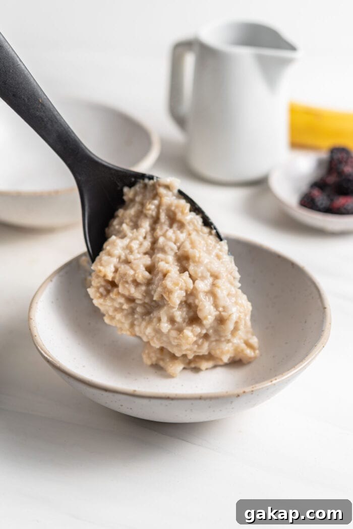 Adding a large scoop of cooked oatmeal to a bowl.