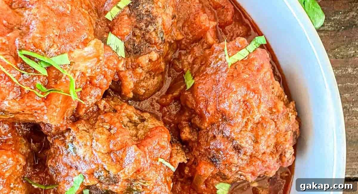 Overhead up close image of dutch oven meatballs in tomato sauce with garnish. 