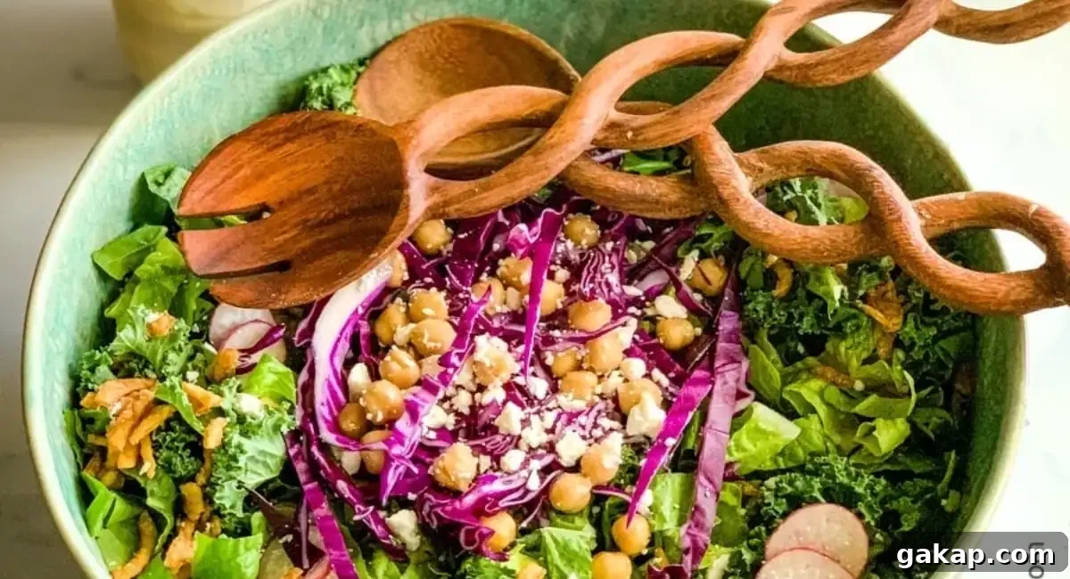 Overhead image of kale crunch salad in green bowl with wooden spoon and salad fork. 