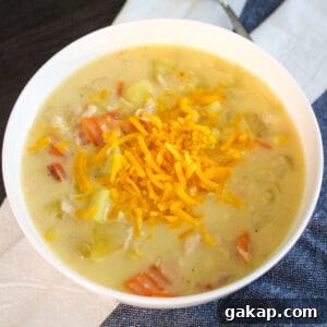 Creamy Slow Cooker Chicken and Potato Chowder 5 A white bowl filled with chicken potato cheese soup on a blue and white kitchen towel.