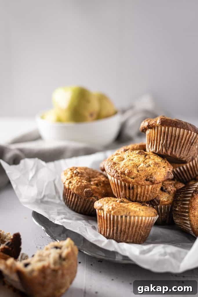 Banana Pear Muffins with Maple Glaze Recipe 3 A side angle view of a plate of pear banana muffins with pears in the background