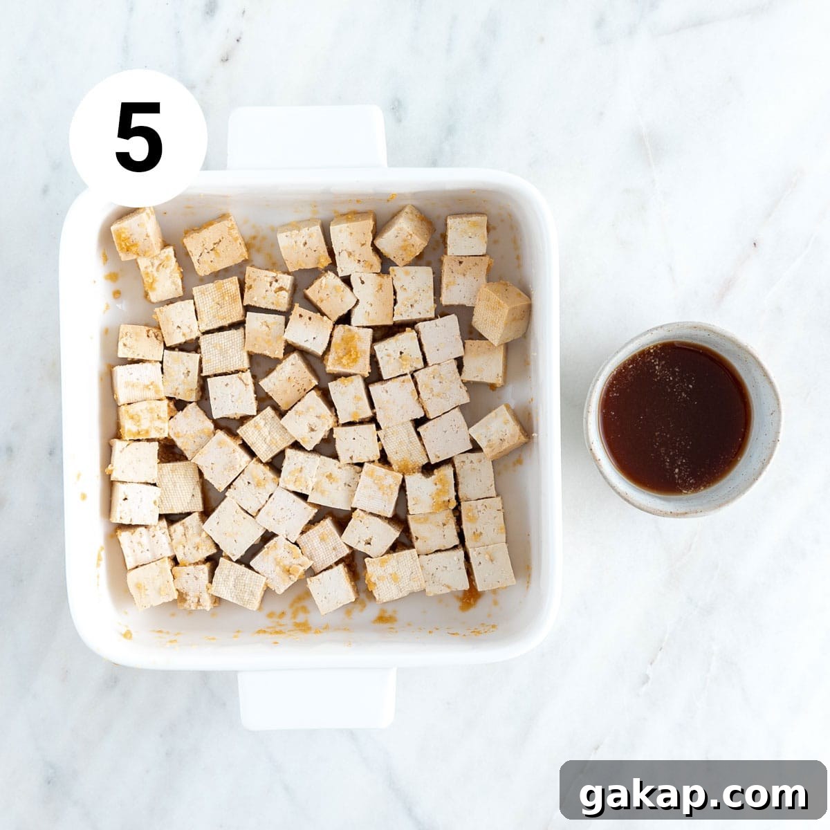 Tofu cubes in a baking dish and marinade in a bowl.