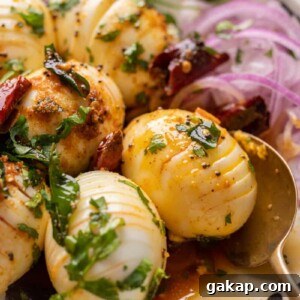 Close up of hasselback egg tadka with a spoon and sliced onions on the side