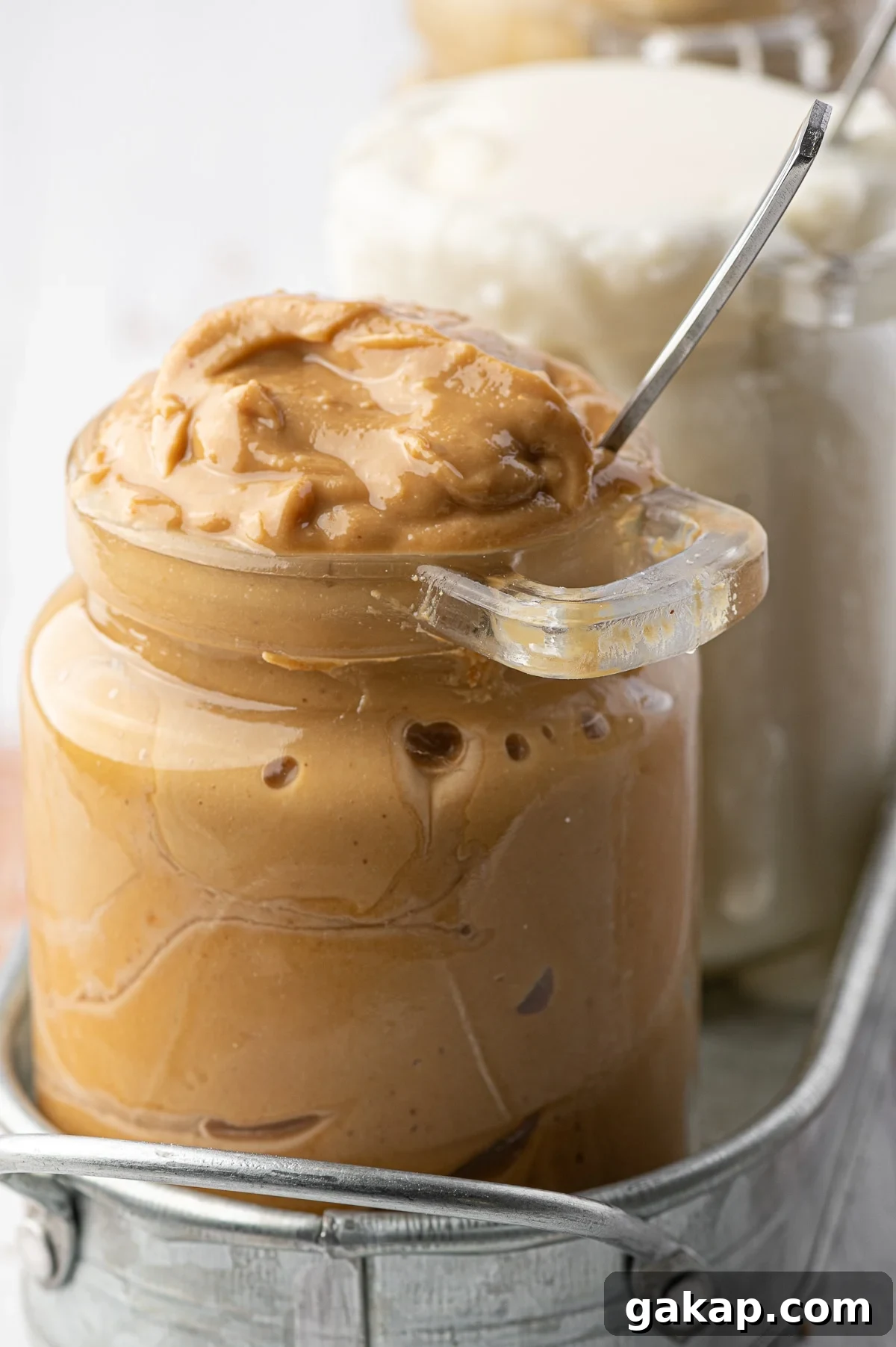 Top Nut Butters for Low-Carb Baking: Almond, Peanut & More 3 An overfull glass jar of homemade natural peanut butter with a metal spoon stuck in the jar.