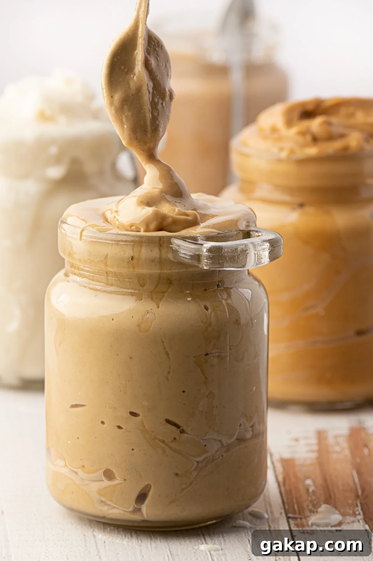 Top Nut Butters for Low-Carb Baking: Almond, Peanut & More 6 A jar of cashew butter being spooned into a glass jar with jars of overfull nut butters in the background