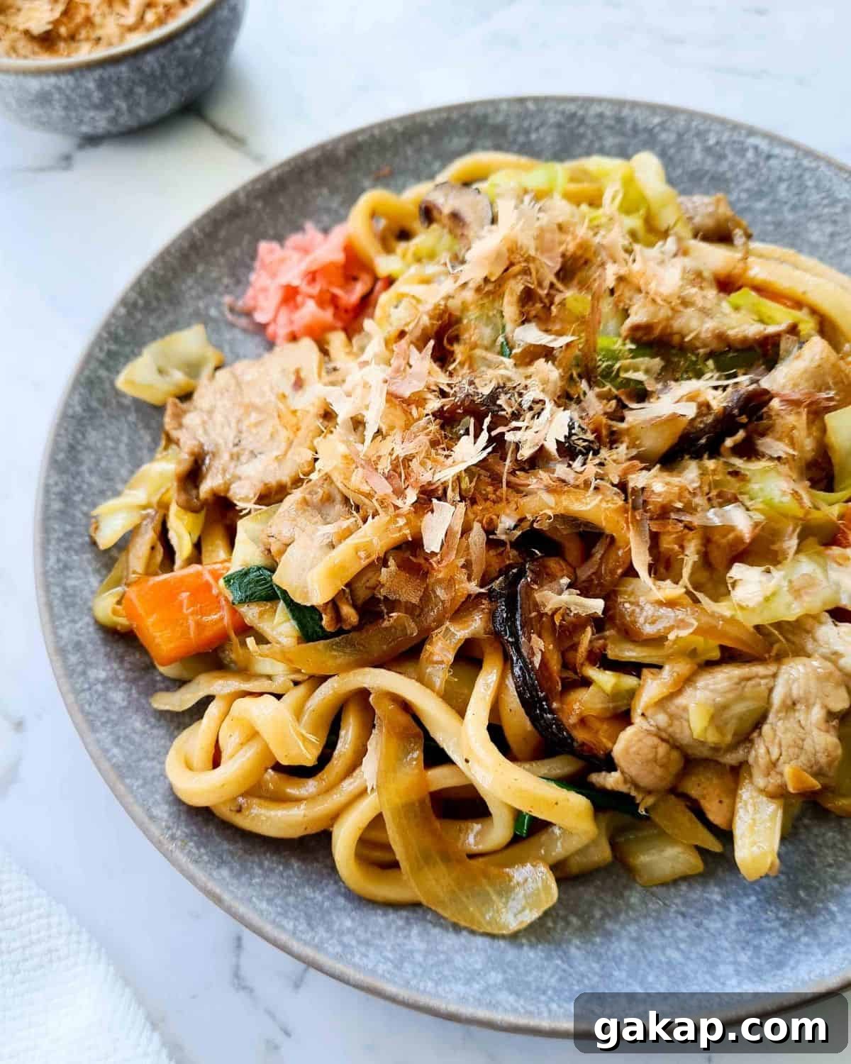 Zoomed in side profile of a plate of noodles sprinkled with bonito flakes 