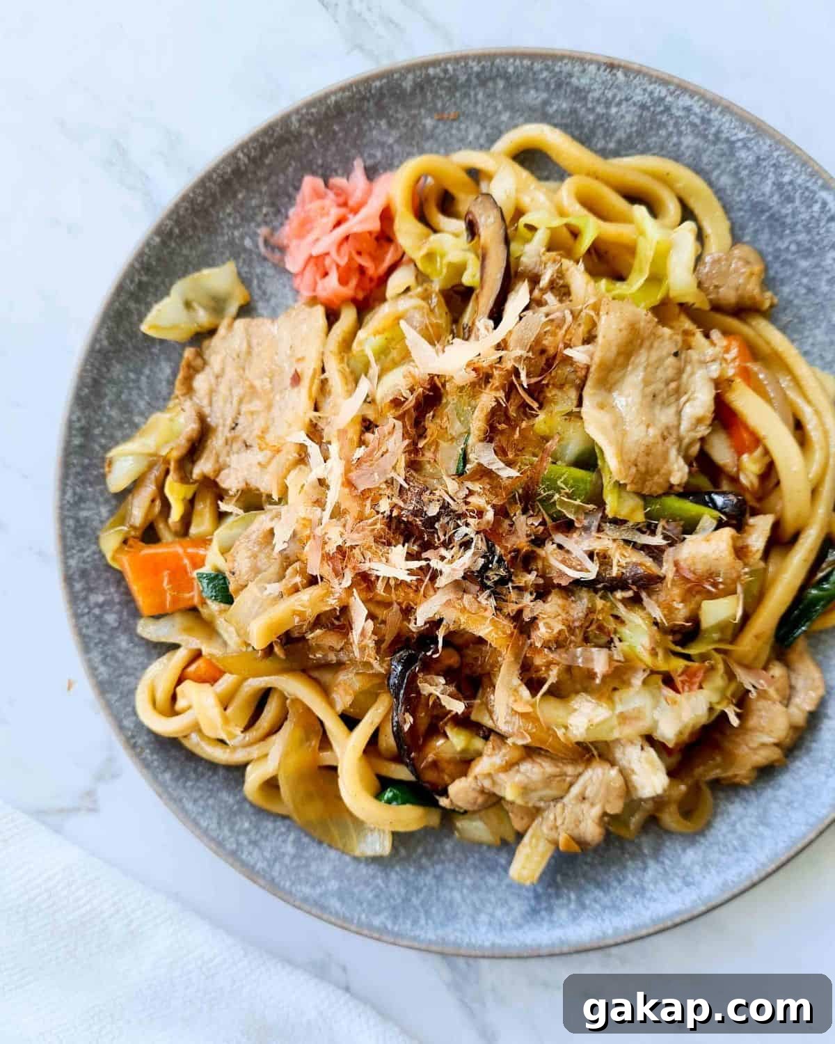 overhead view of a plate of noodles sprinkled with bonito flakes and pickled ginger on the side 