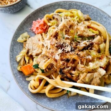 Side view of a plate of udon stir fry with chopsticks