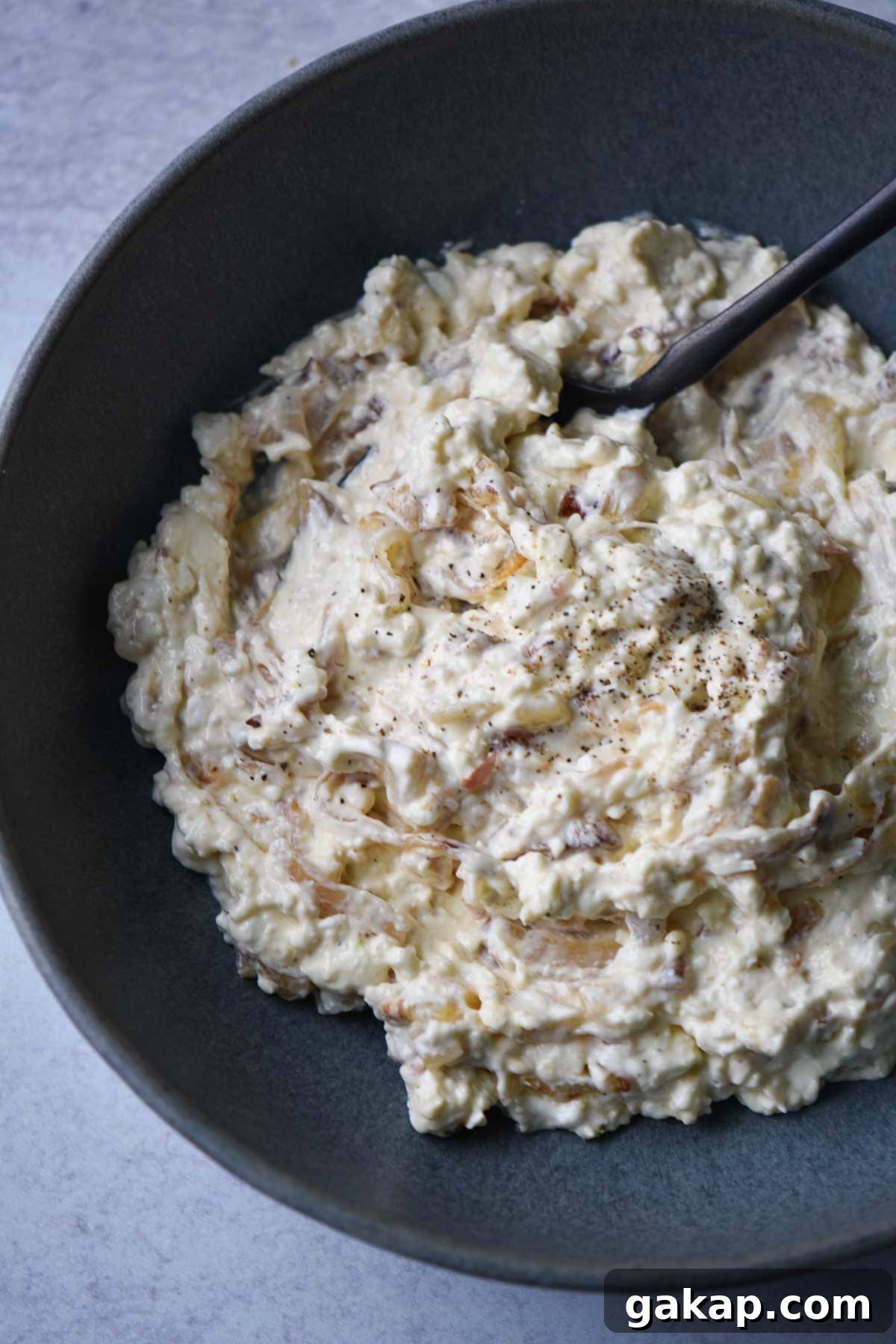 Creamy Caramelized Shallot Dip Recipe for Parties 5 A creamy shallot dip in a black bowl with a black spoon dipping in