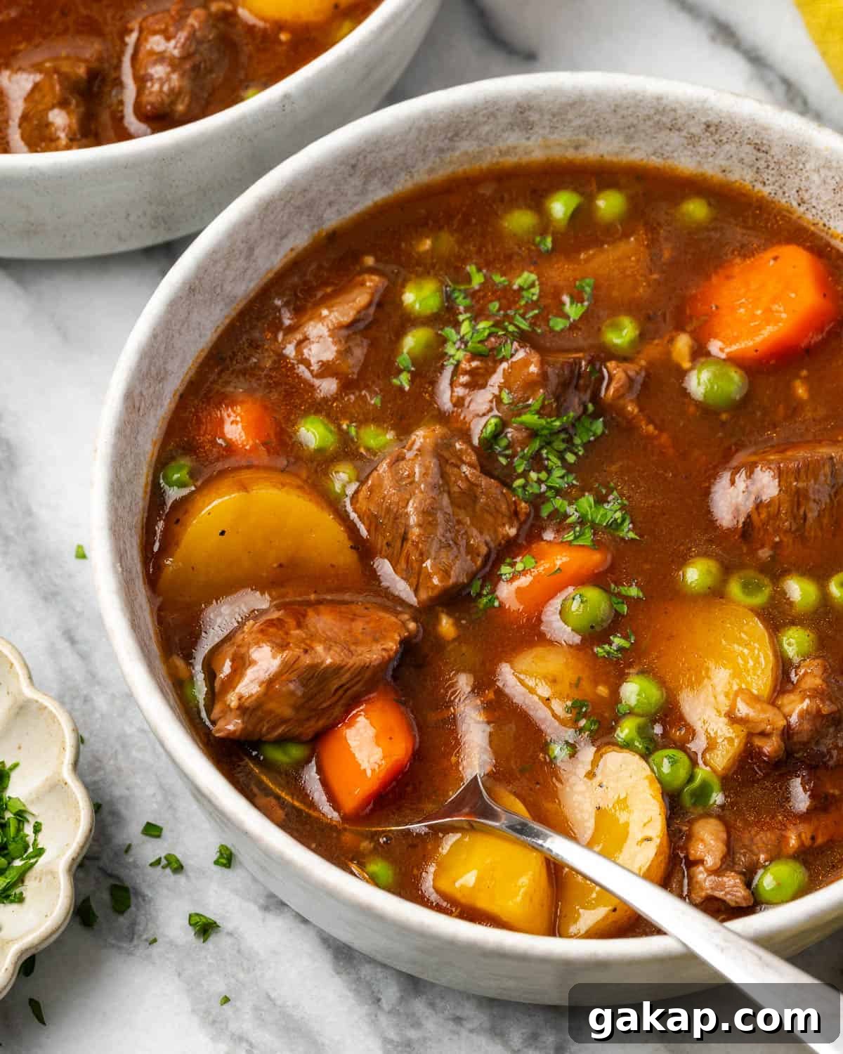 A spoon scooping a bite of beef stew from a ceramic bowl. 