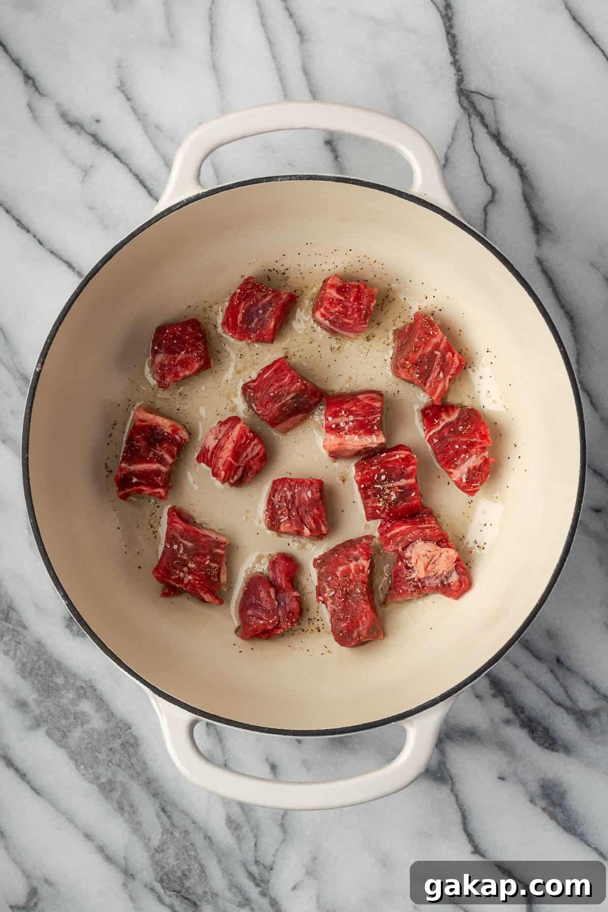 Bite sized pieces of chuck roast cooking in a Dutch oven pot. 