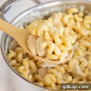 A wooden spoon scooping chicken Alfredo pasta from a stainless steel pot.
