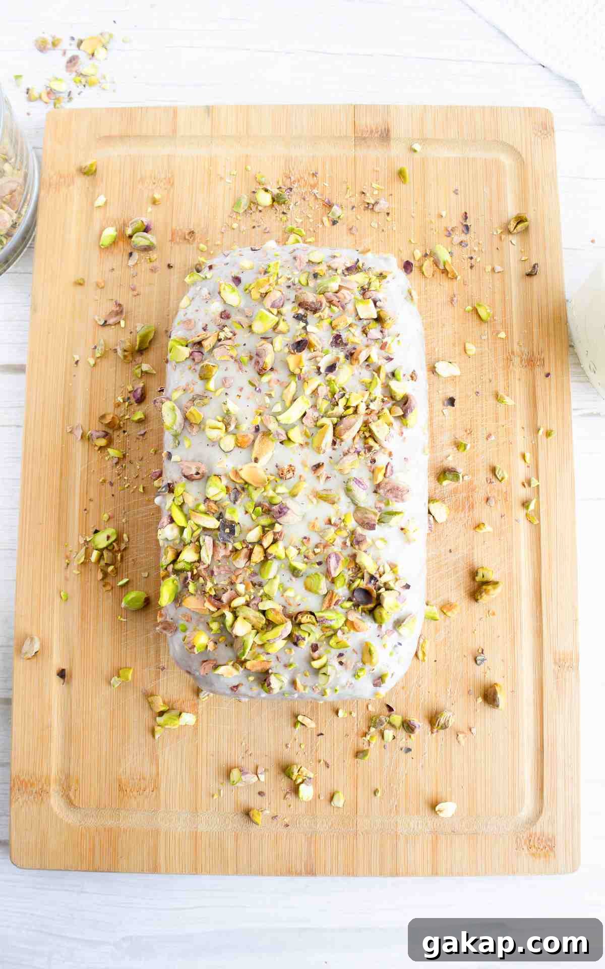 Pistachio Quick Bread Recipe: Moist Loaf with Crunchy Nuts 4 An uncut iced pistachio bread loaf on a wooden serving board.
