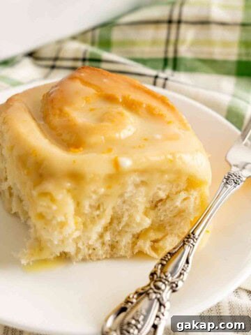 A sweet orange roll on a plate with a decorative fork.