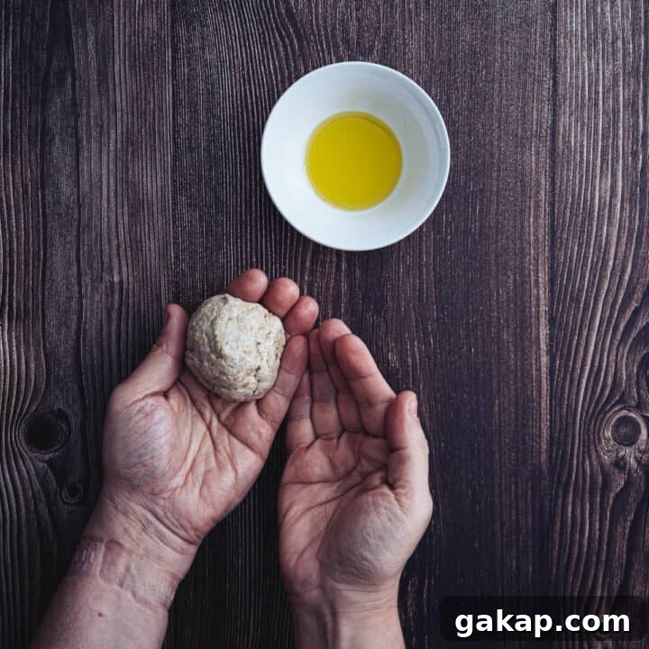 two hands holding buckwheat pita bread dough shaped into a ball with olive oil.