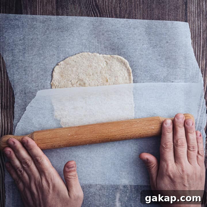 rolling out buckwheat pita bread between two sheets of parchment on a wooden surface.
