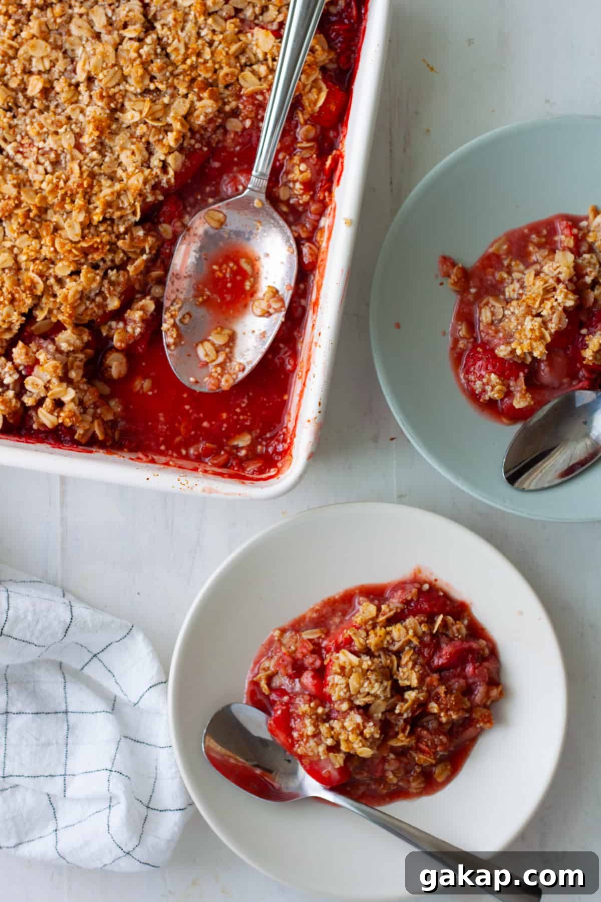 Two plates of strawberry crumble and a baking dish with more crumble off to the side.