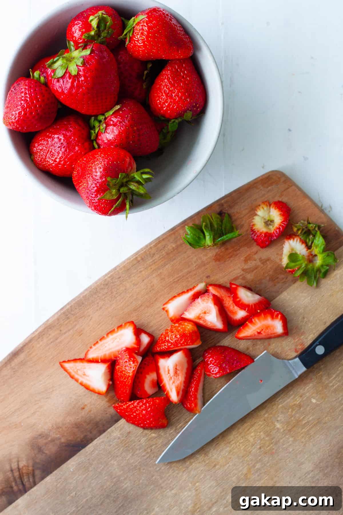 Strawberries getting cut on a wooden cutting board.