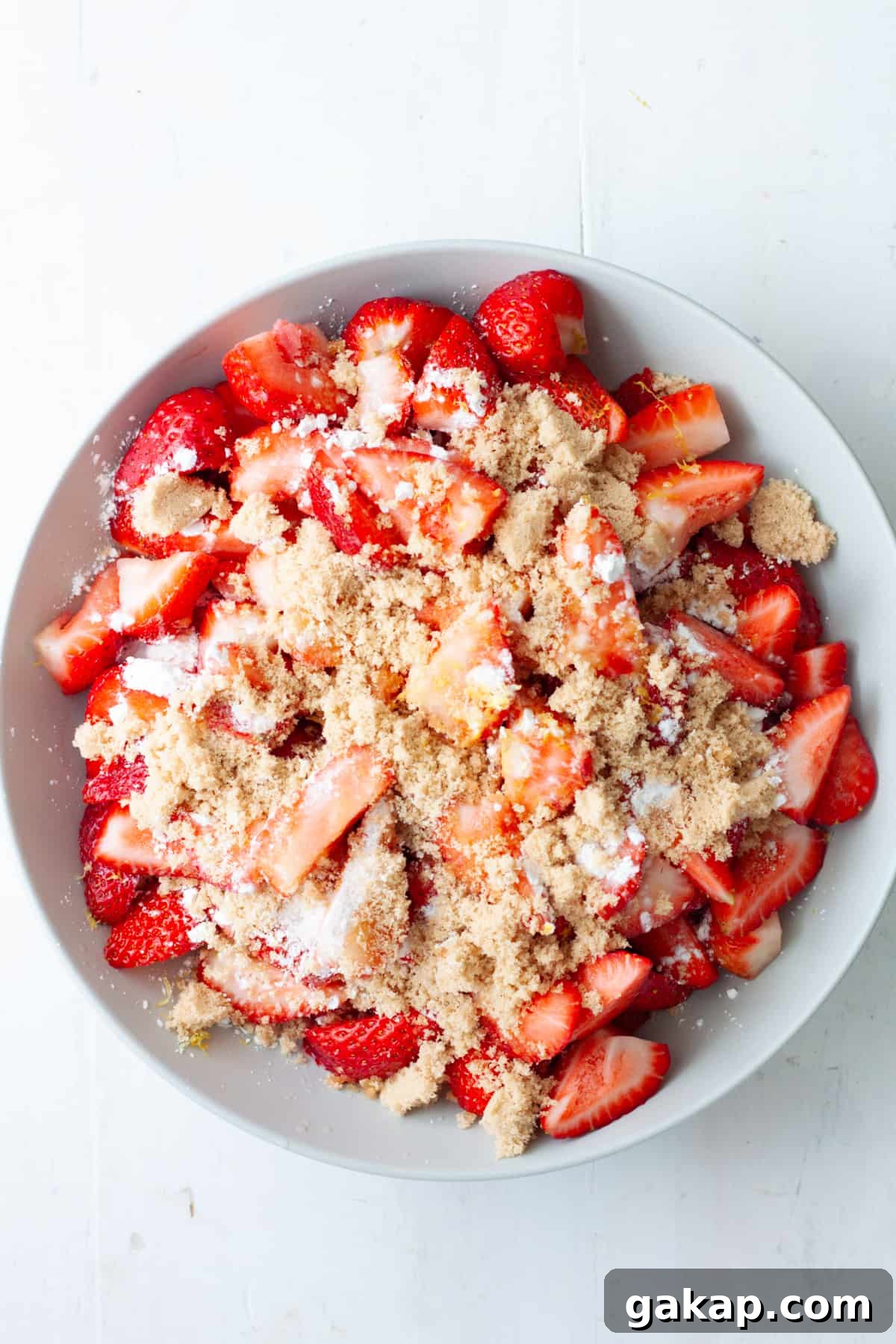 Sliced strawberries in a mixing bowl with sugar and lemon juice on top.