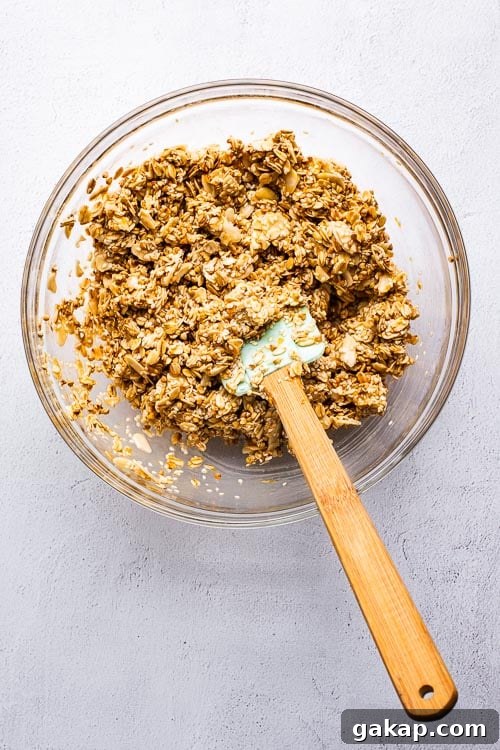 Tahini Sesame Granola with Honey and Orange Zest 5 Tahini orange granola ingredients mixed in a glass bowl with a spatula.