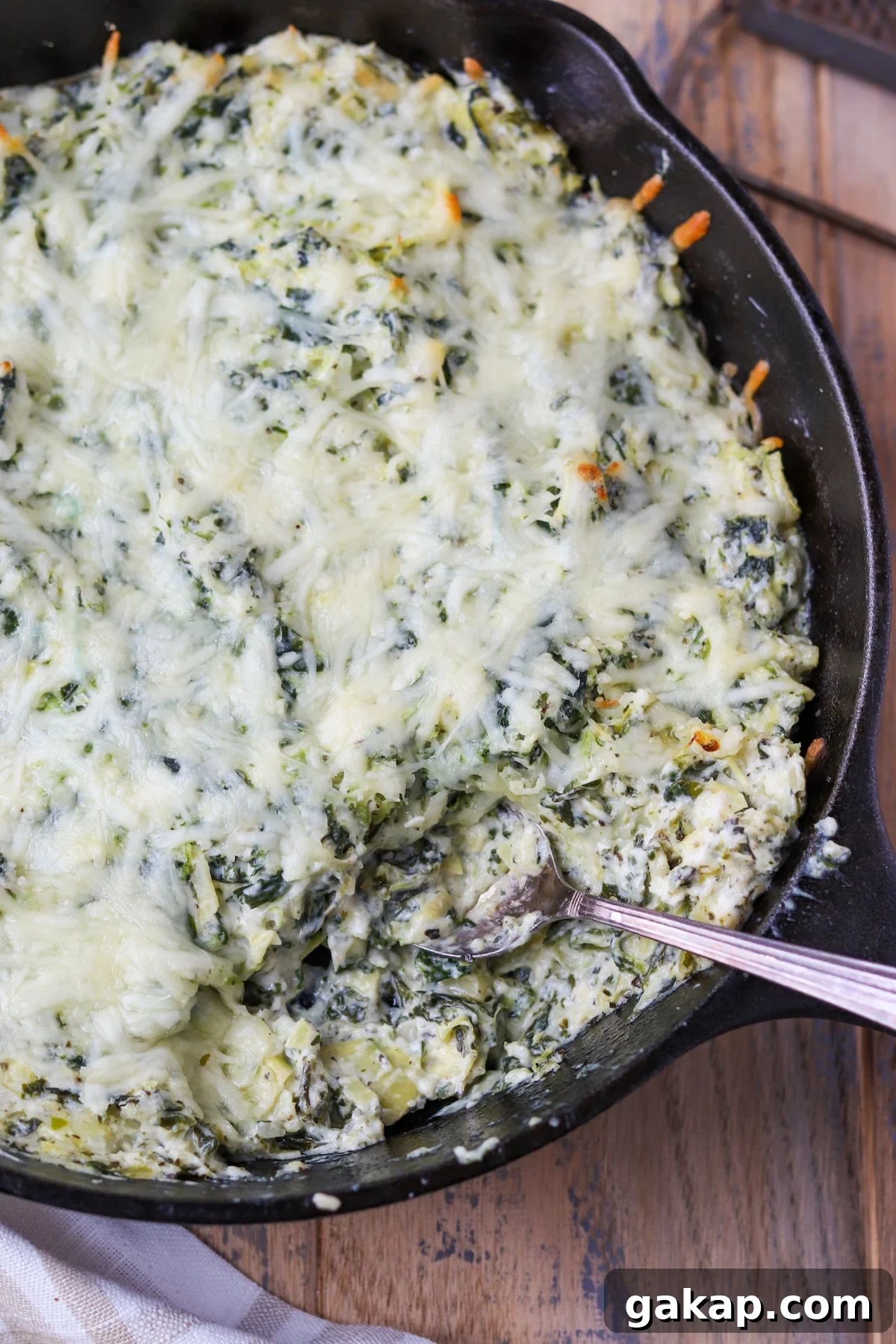 cast iron skillet with prepared spinach artichoke dip, melty cheese on top and creamy texture