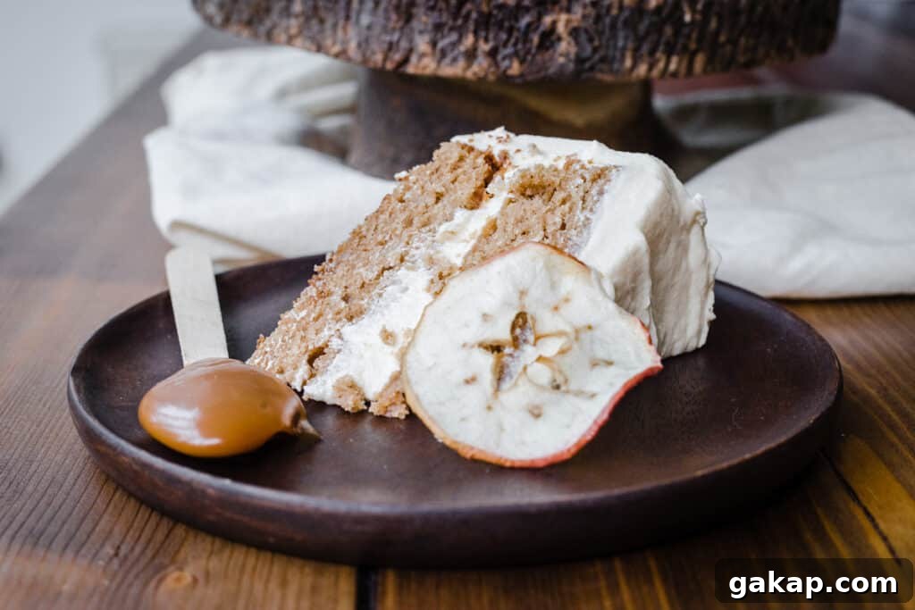 A slice of Cinnamon Apple Cake with Salted Caramel Cream Cheese Buttercream on a wooden plate with an apple slice and a spoon of caramel