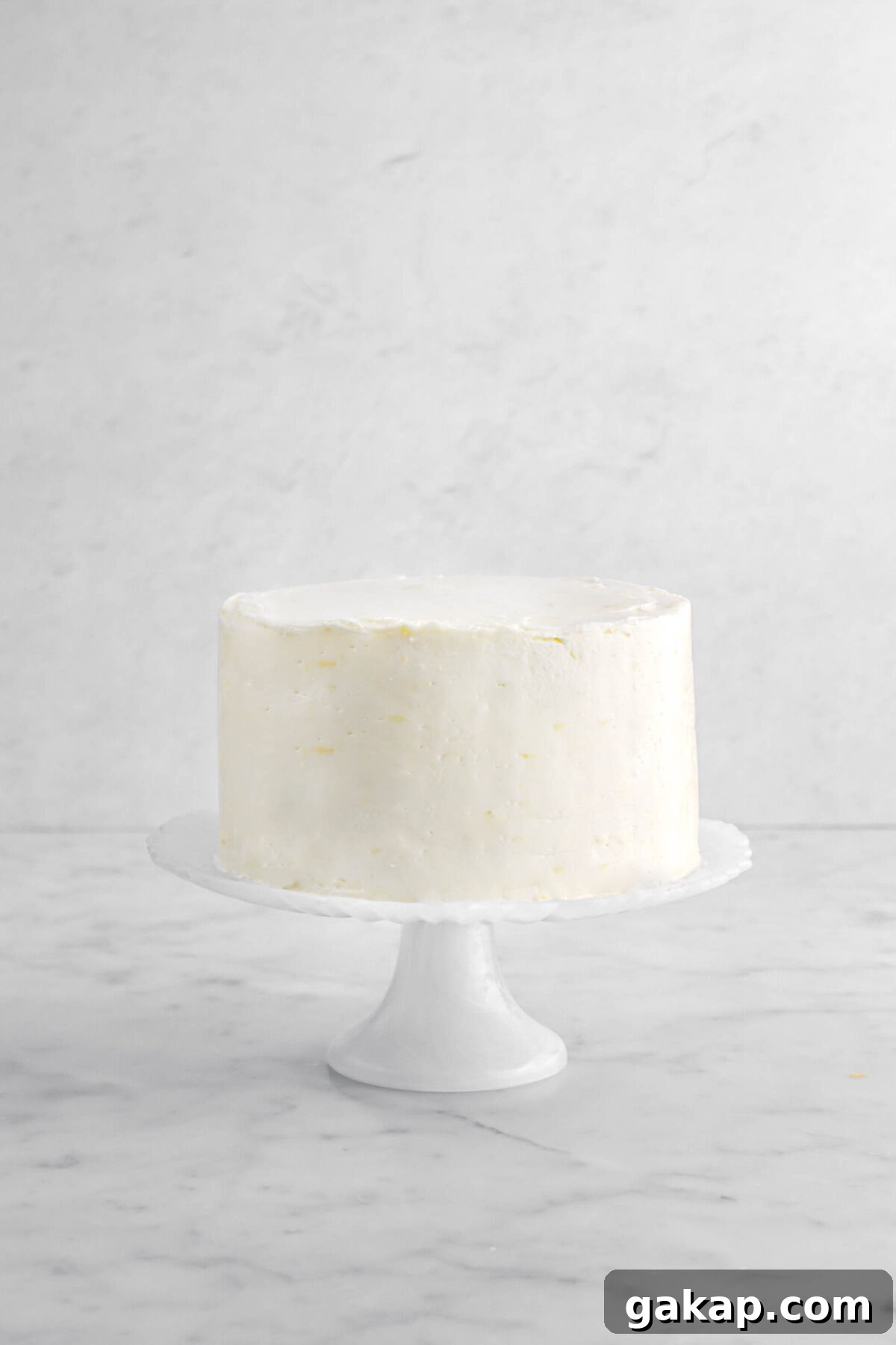 Lemon Blueberry Layer Cake with Zesty Lemon Buttercream 14 Frosted cake on white cake plate on marble surface.
