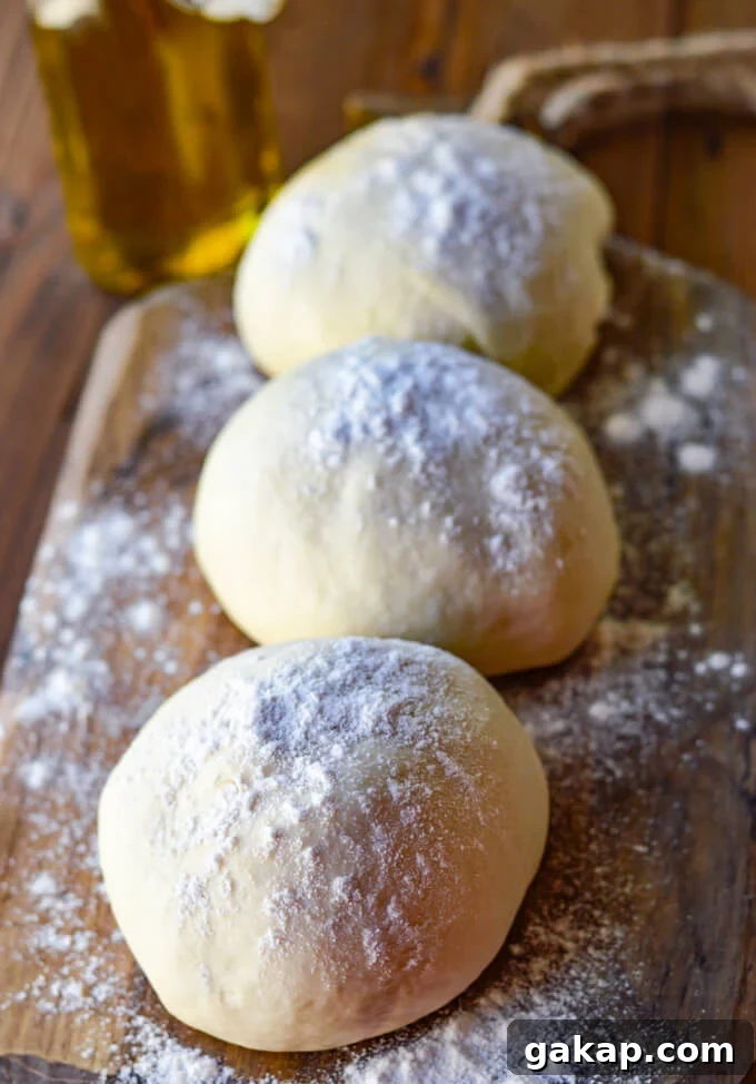Crispy-Chewy Homemade Pizza Dough Recipe for Perfect Crust 2 Three balls of pizza dough rest on a floured wooden board with olive oil in the background.