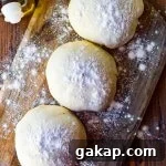 Three balls of pizza dough rest on a floured wooden board with olive oil in the background.