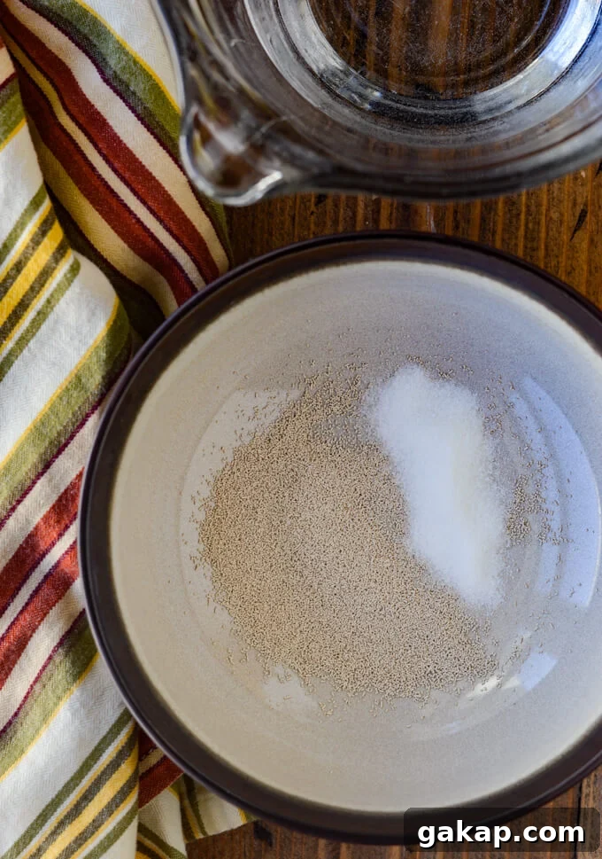 Crispy-Chewy Homemade Pizza Dough Recipe for Perfect Crust 3 A bowl of yeast with sugar next to a measuring bowl of water and a striped napkin.