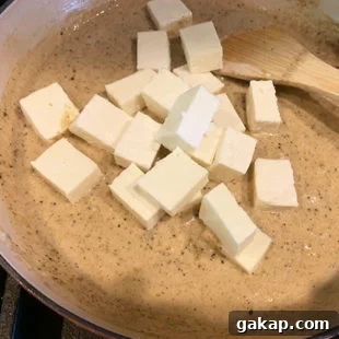 Black Pepper Paneer (Paneer Kali Mirch) — Spicy Indian Cottage Cheese 17 paneer cubes being added to a cream colored sauce in a pan