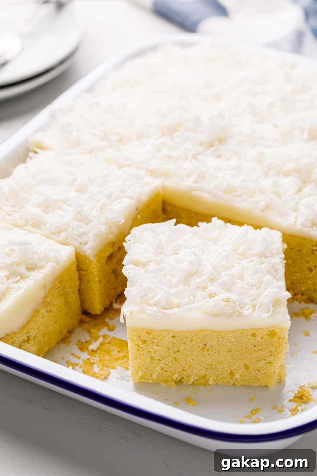 Classic Coconut Cake Recipe for Moist, Creamy Layers 3 square slice serving of coconut cake with coconut cream frosting in a 9x13 inch baking pan