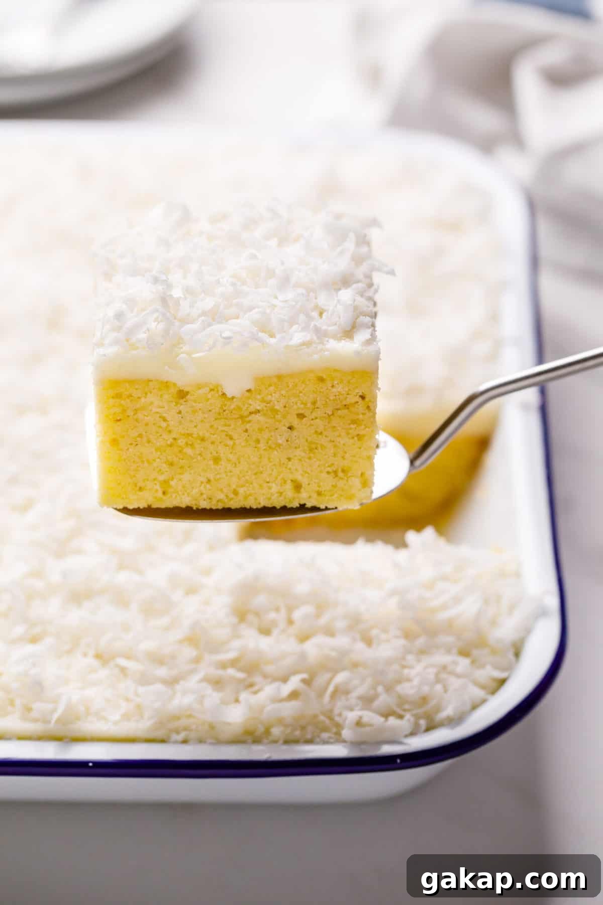 Classic Coconut Cake Recipe for Moist, Creamy Layers 6 square slice serving of coconut cake with coconut cream frosting sitting on a metal spatula