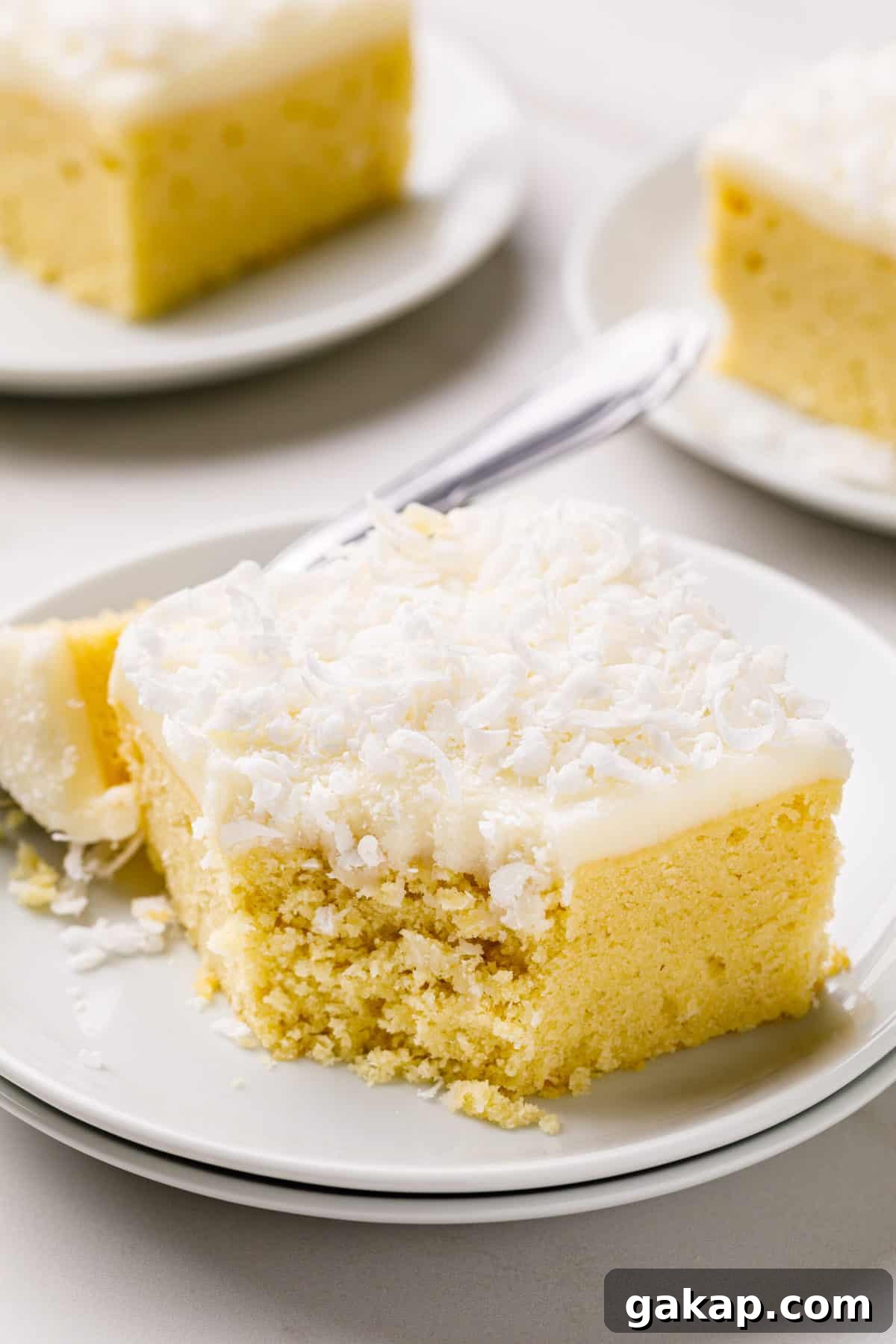 Classic Coconut Cake Recipe for Moist, Creamy Layers 7 coconut cream frosting on a square slice of coconut cake served on a white round plate
