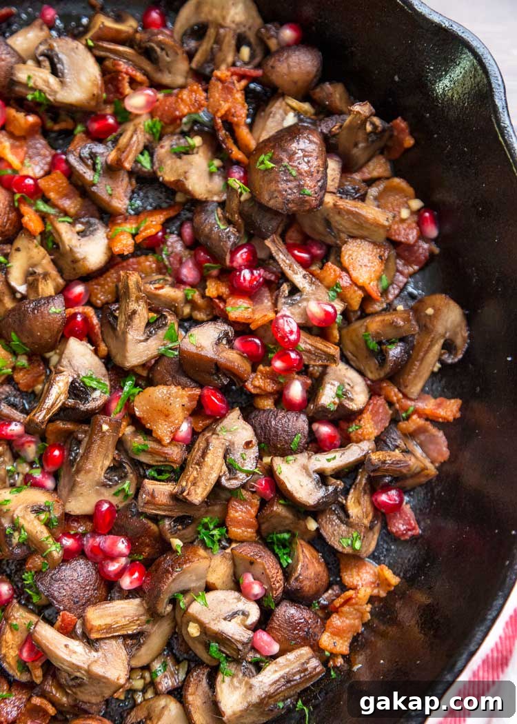 overhead closeup: my roasted mushroom recipe in a skillet with herbs, pomegranate arils, and bacon