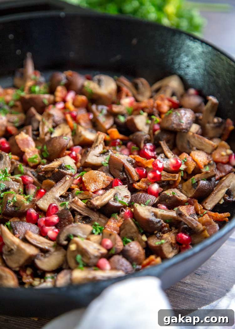side view closeup: roasted mushrooms in a skillet with bacon, pomegranate arils, and fresh herbs