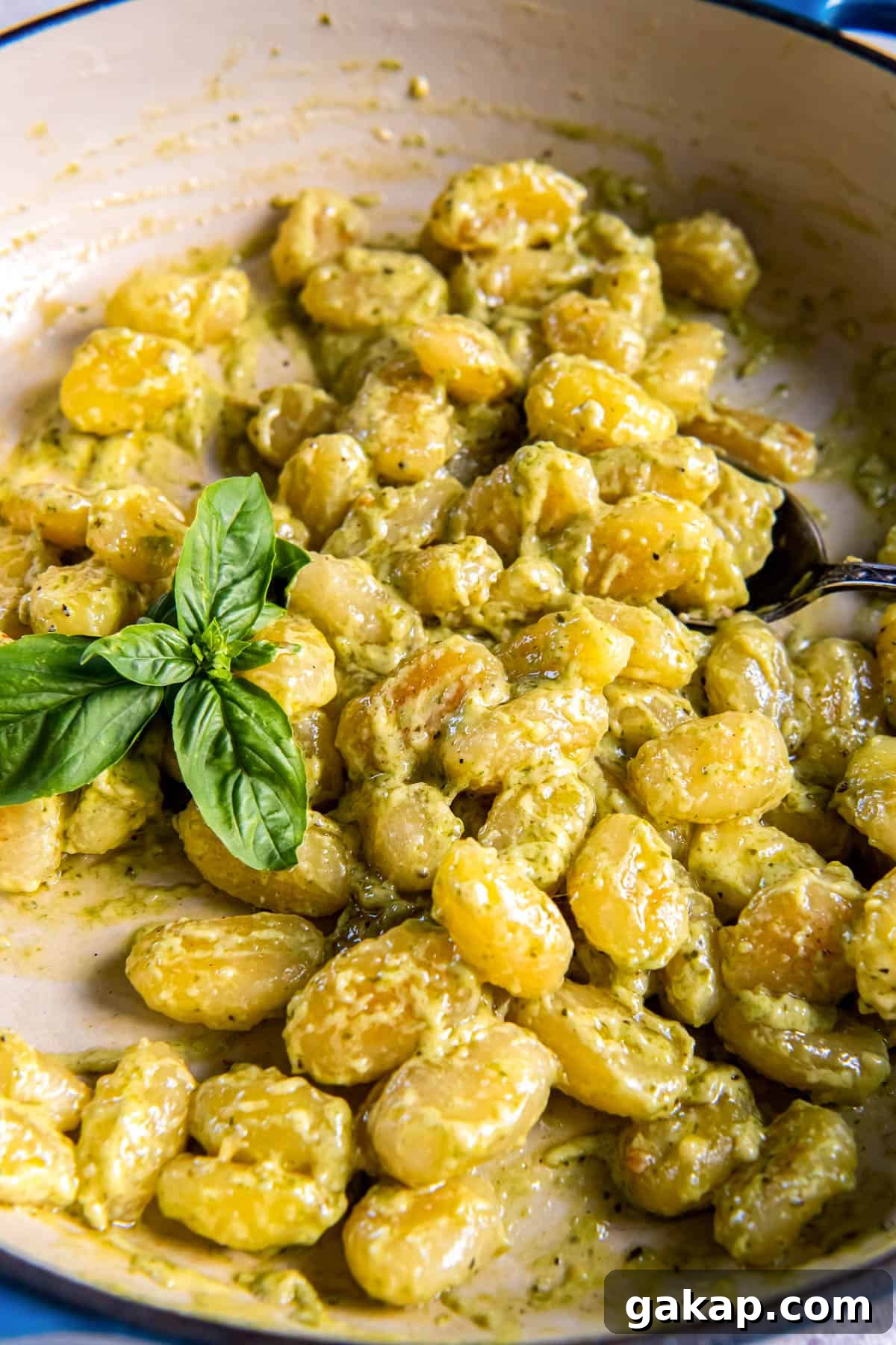 Creamy pesto gnocchi in a skillet ready for serving. A piece of fresh basil sits on top of the pasta for garnish.