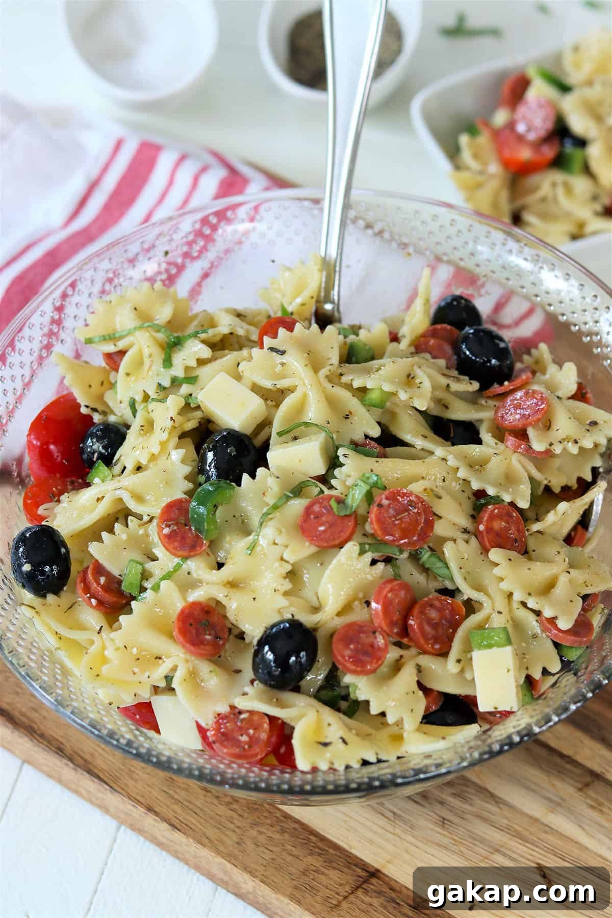 A clear glass bowl full of italian pasta salad garnished with fresh basil