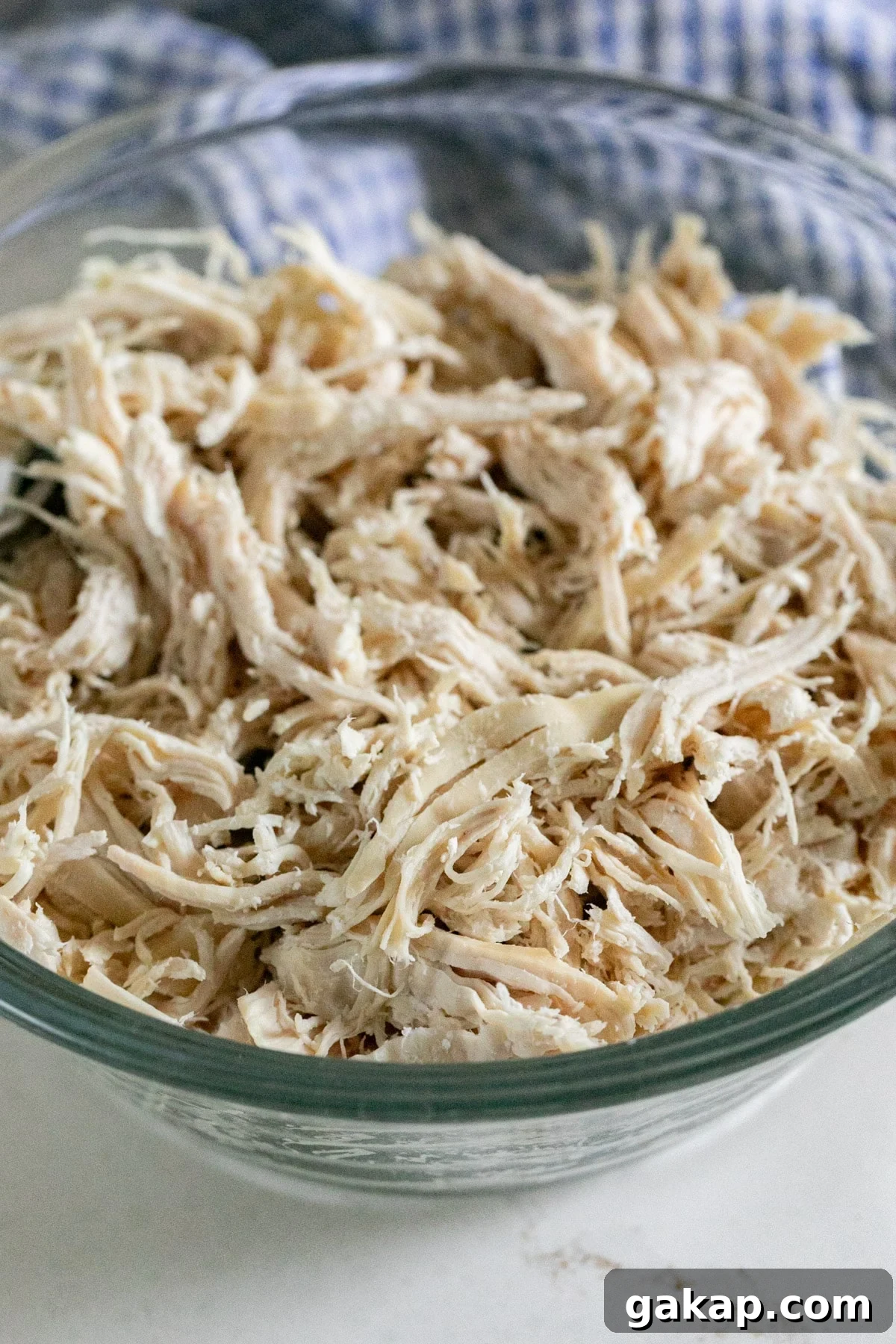A close up image of shredded chicken breast in a glass bowl.