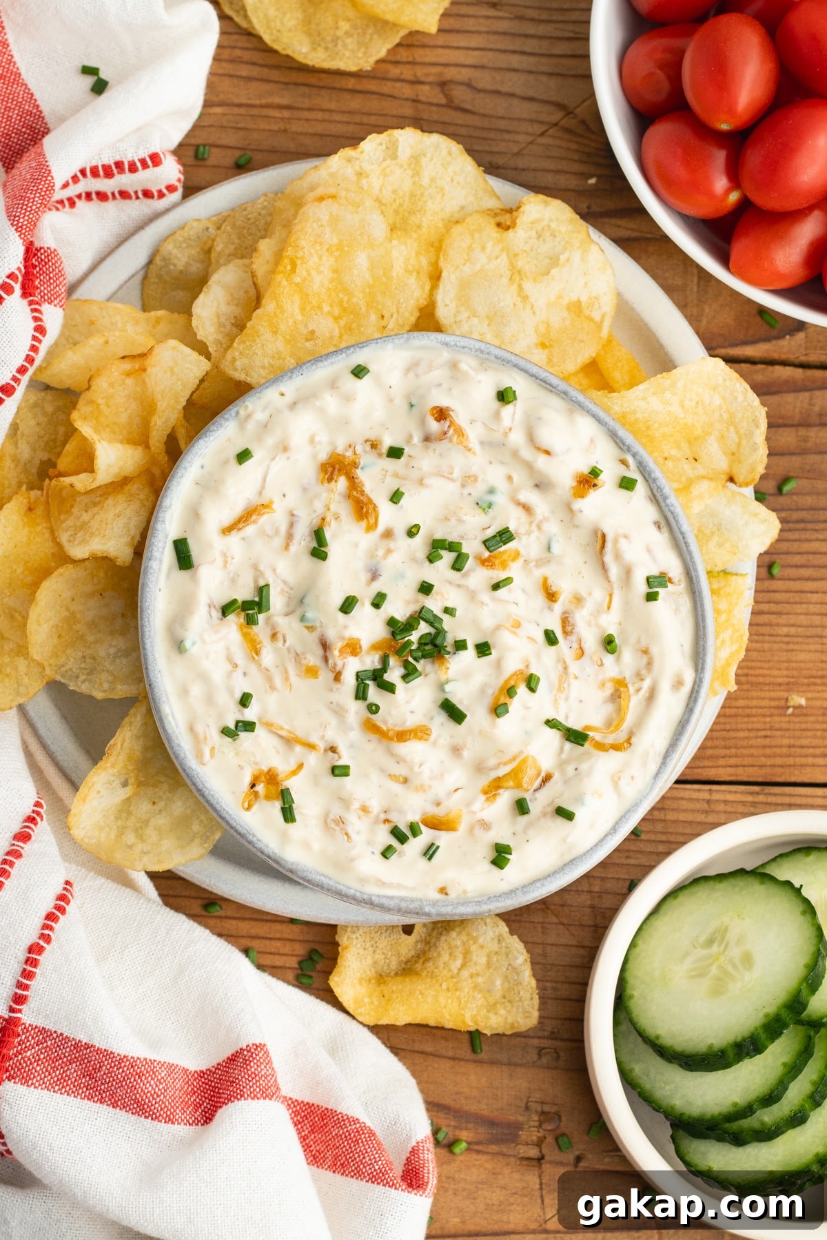 This is a picture of a bowl with the onion dip, chips, tomatoes and cucumber.