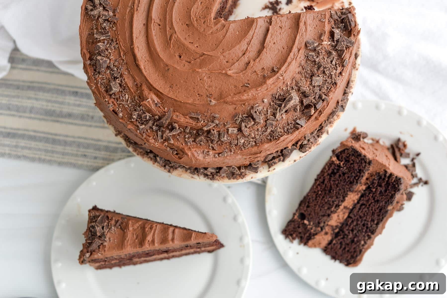 Sourdough chocolate layer cake topped with smooth chocolate frosting and chocolate shavings, with two slices served on white plates beside the cake.