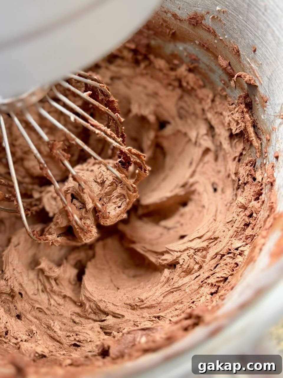 Chocolate frosting being whipped in a stand mixer bowl until light and fluffy.