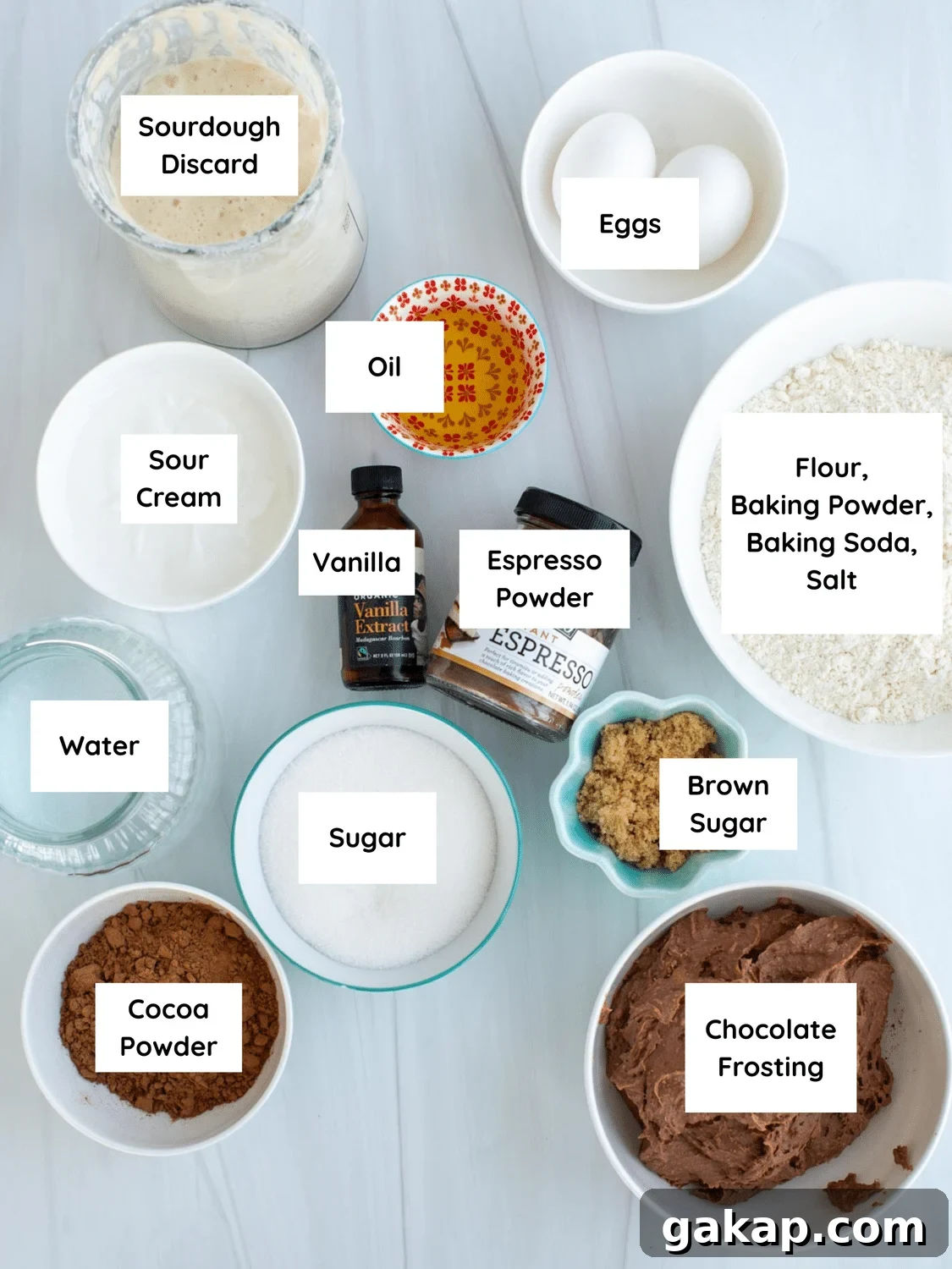 Ingredients on the counter include sourdough discard, eggs, oil, sour cream, vanilla, espresso powder, flour, baking powder, baking soda, salt, brown sugar, sugar, water, cocoa powder, and chocolate frosting.