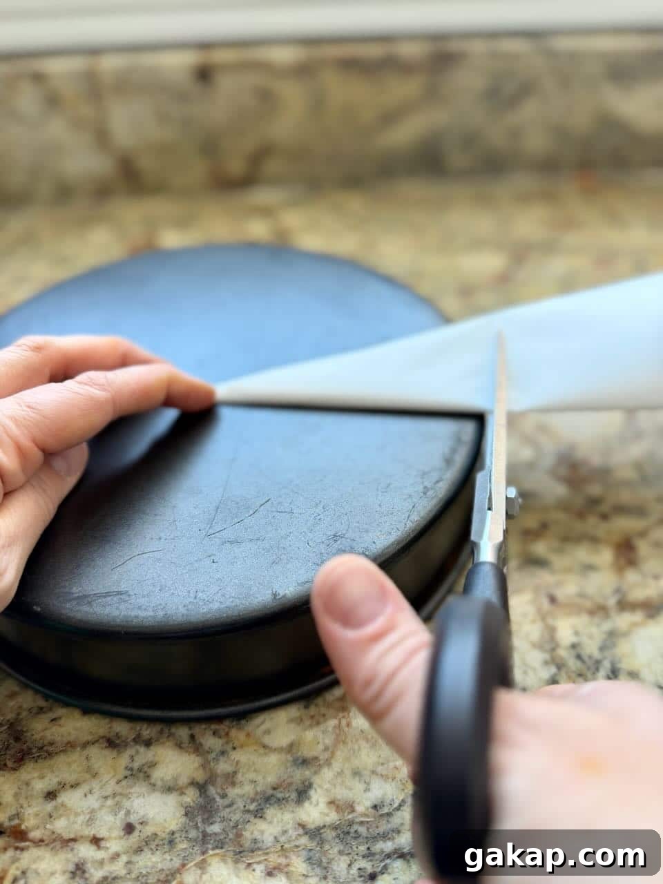 Cutting parchment paper to size using scissors and a round cake pan as a guide.