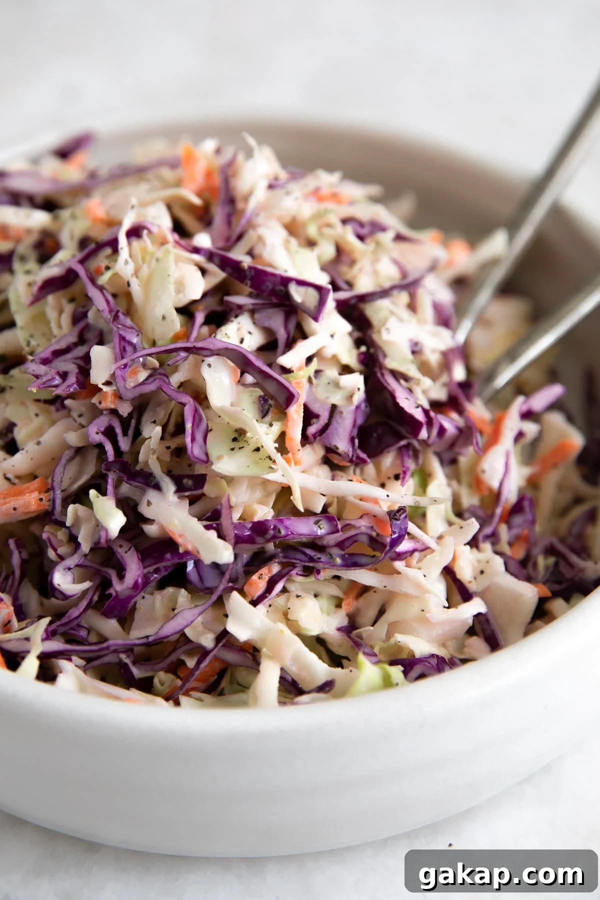 A large white serving bowl filled with freshly made creamy coleslaw, featuring a mix of green and purple cabbage and shredded carrots, dressed in a homemade mayonnaise-based dressing.