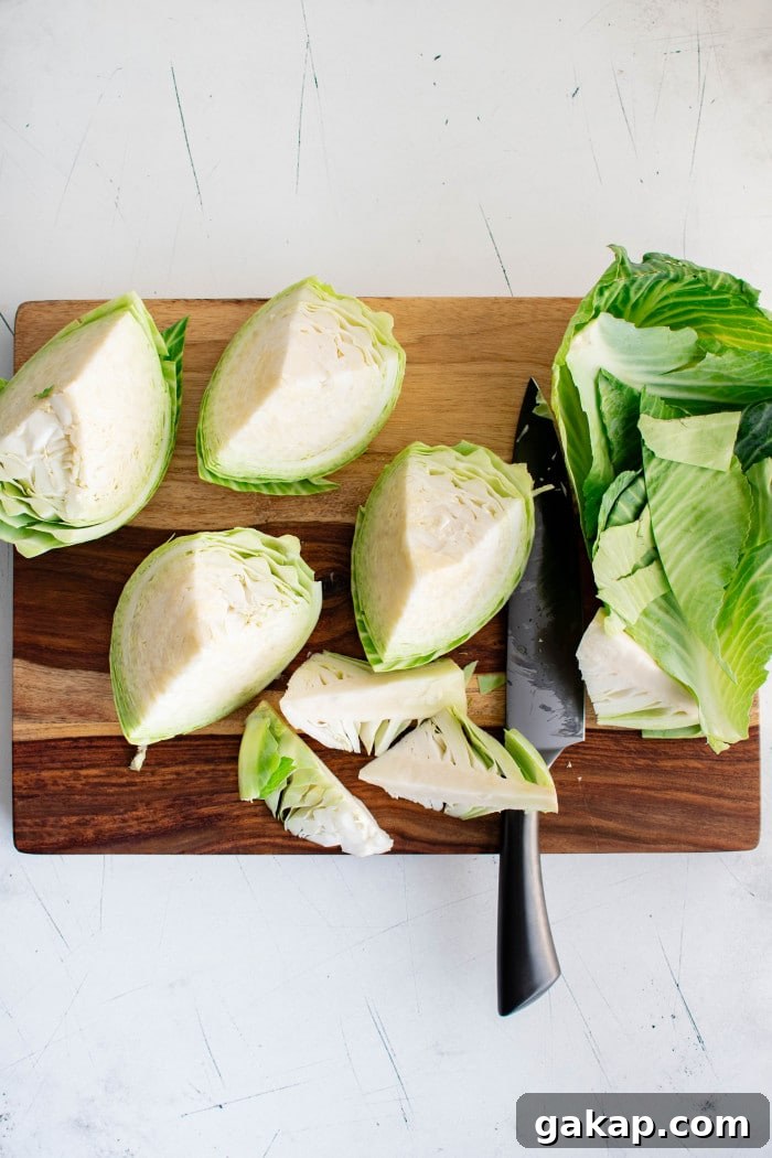 A large head of green cabbage cut into wedges with the outer leaves removed, shown on a wooden cutting board with a black-handled chef’s knife.