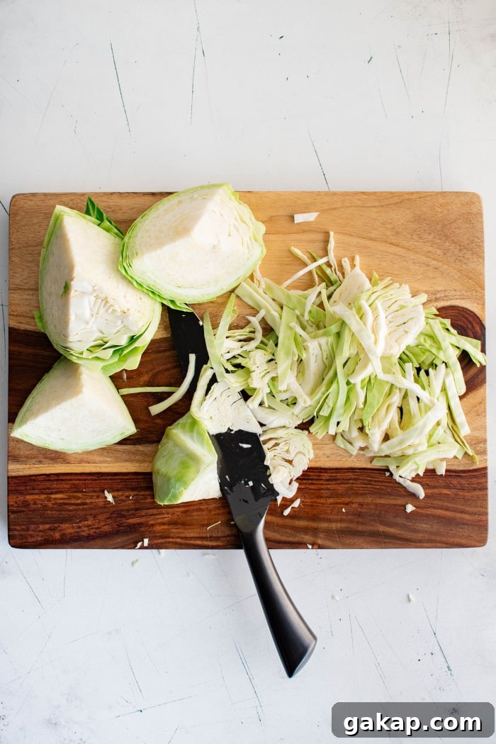 Slicing green cabbage into thin strips on a cutting board.