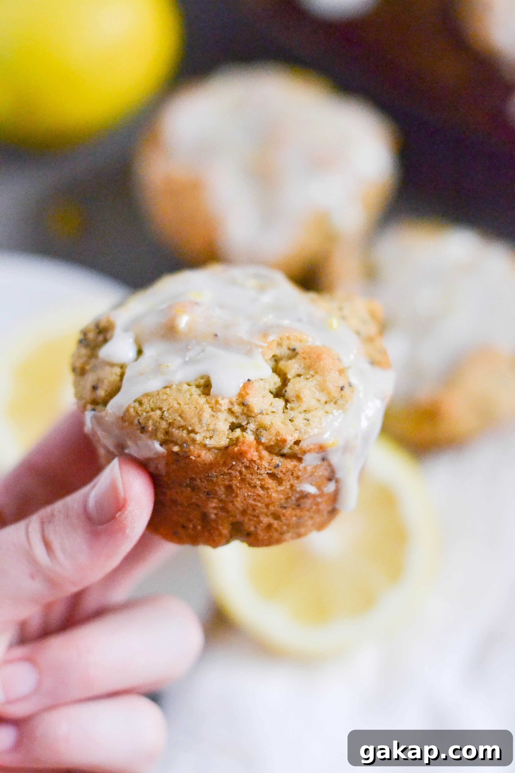 Gluten-Free Vegan Lemon Poppy Seed Muffins Recipe 4 A hand holding a vegan gluten-free lemon poppyseed muffin with lemon glaze on it.